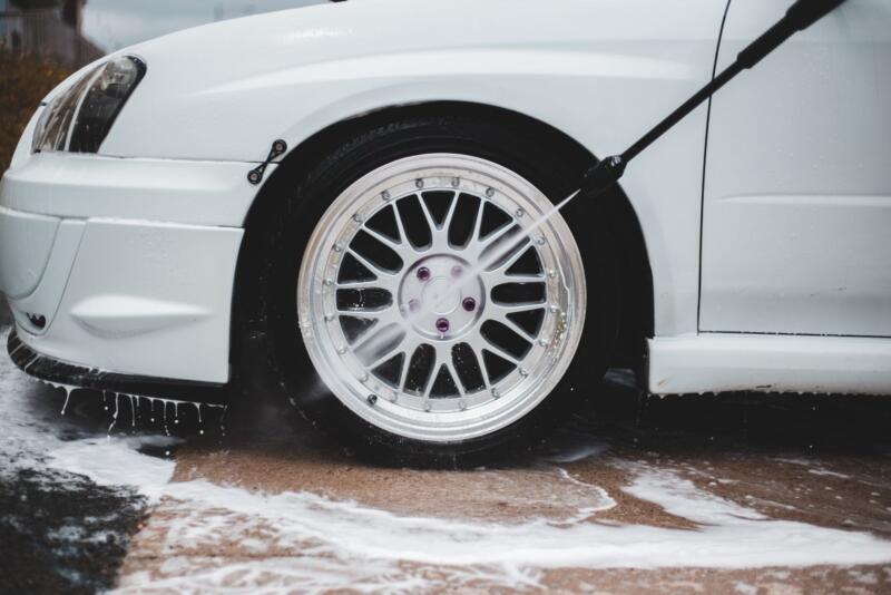 Lanza de una hidrolimpiadora limpiando la llanta de un coche con espuma