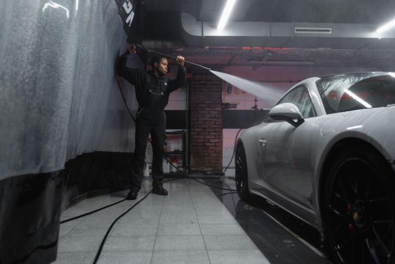 Hombre lavando un coche blanco con una hidrolimpiadora en un túnel de lavado