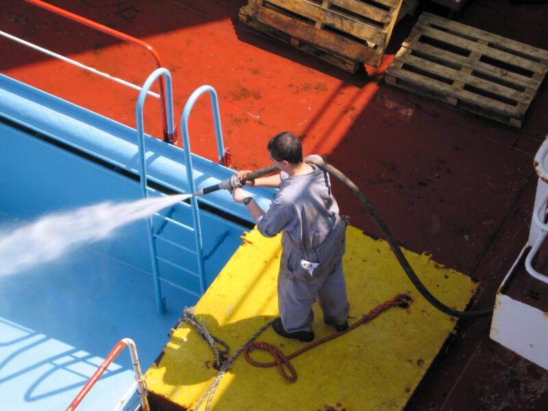 Operario limpiando la cubierta de un barco con una manguera a alta presión